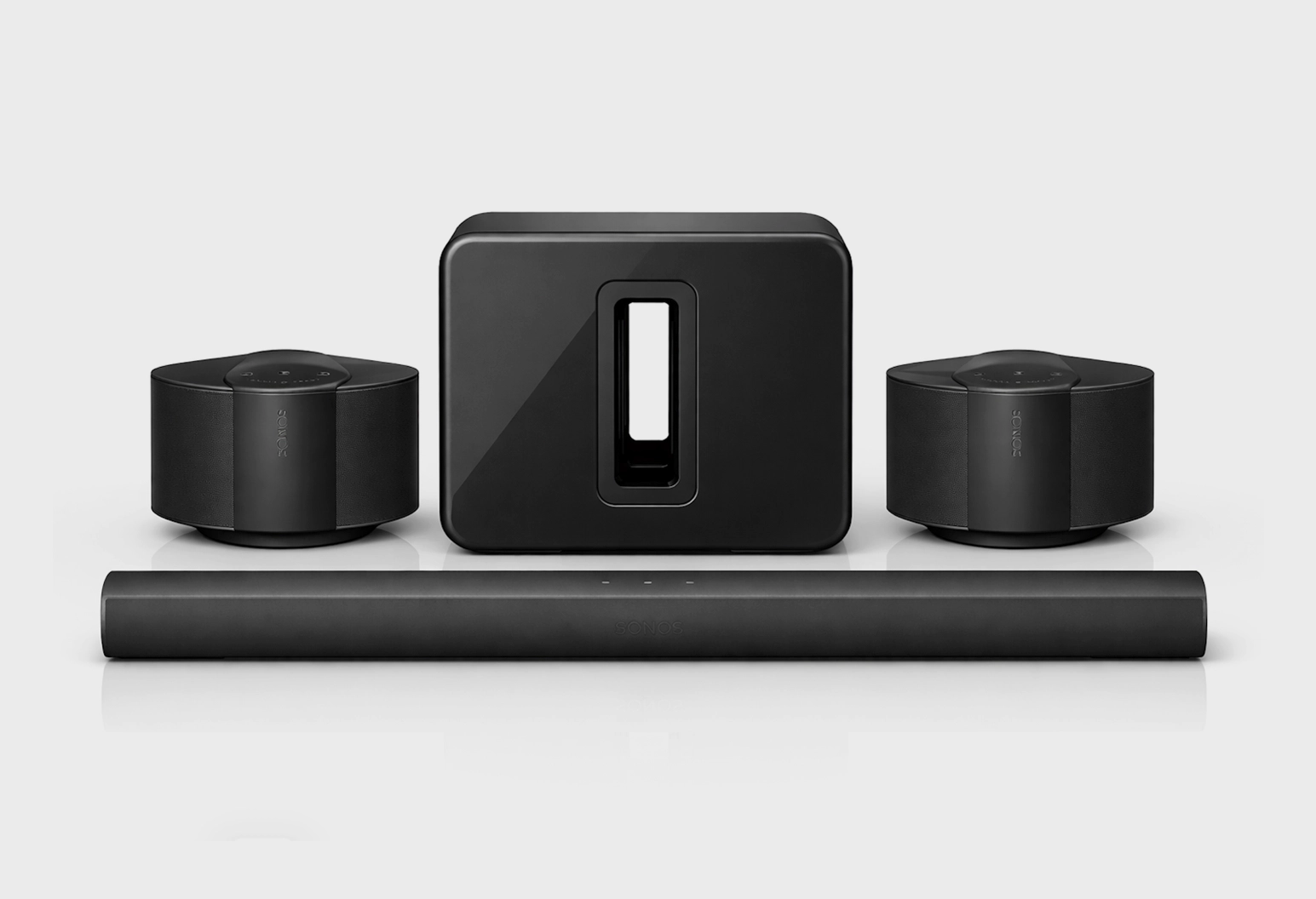 Un système d'enceintes home cinéma noir comprenant une barre de son fine à l'avant, un caisson de basses rectangulaire doté d'une découpe rectangulaire centrale à l'arrière, et deux enceintes rondes à sommet plat (équipées de boutons de commande sur le dessus) placées de part et d'autre du caisson de basses, le tout reposant sur une surface réfléchissante devant un fond gris clair.