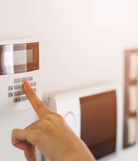 La main d'une personne appuyant sur une touche d'un clavier d'alarme de sécurité blanc fixé au mur.